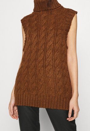Pull marron sans manches à col roulé en maille torsadée porté avec un pantalon noir, montrant le torse et les bras sans tête visible.