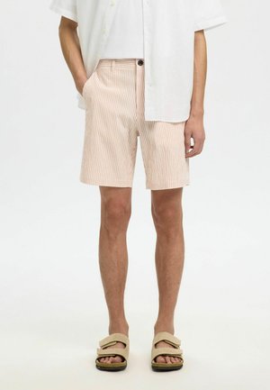 Pantalones cortos a rayas en mezcla de algodón rosa claro y blanco, con bolsillos laterales, cierre de botones y un ajuste relajado. Combinados con sandalias marrones.