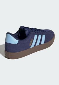 Marinblå mockaskor med ljusblå detaljer, har tre ränder på sidan, brun gummisula och en vadderad krage för komfort.