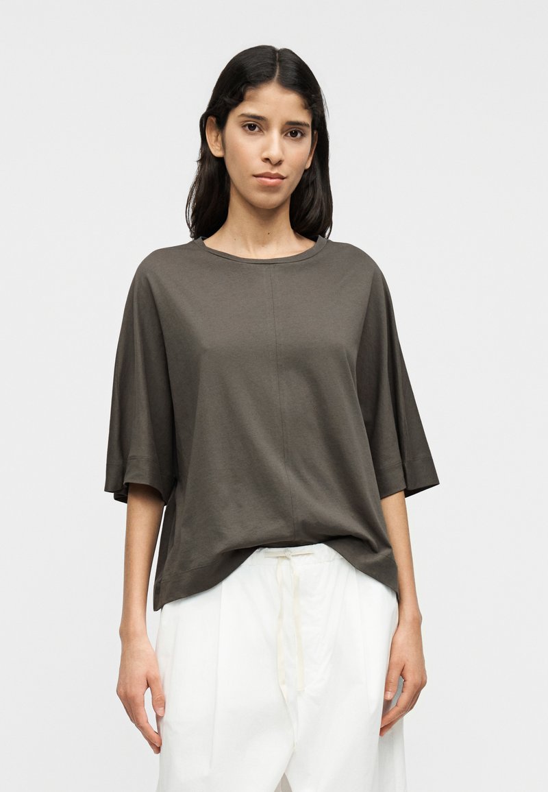 Σκούρο γκρι, άνετο μπλουζάκι με κοντά μανίκια και στρογγυλή λαιμόκοψη· λεία υφή, ελάχιστες ραφές· συνδυασμένο με λευκό παντελόνι.