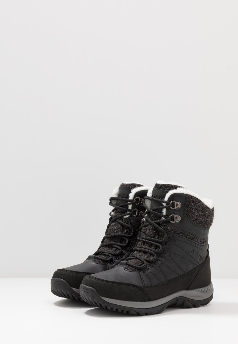 Botas de invierno negras que cuentan con un cuello acolchado, tela gris texturizada, diseño con cordones y una suela de goma resistente para un mejor agarre.