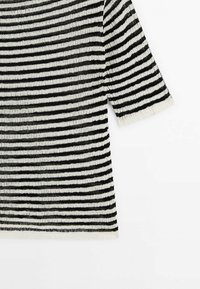 Svart och vit horisontellt randig stickad tröja med trekvartslånga ärmar och ribbad mudd, liggande platt på en vit bakgrund.