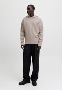 Sudadera de lana beige con un escote amplio, combinada con pantalones negros a rayas y zapatos negros de suela gruesa. Diseño sencillo y corte relajado.