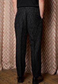 Black trousers with a textured design, featuring two back pockets and side pockets. Cut straight with a polished finish.
