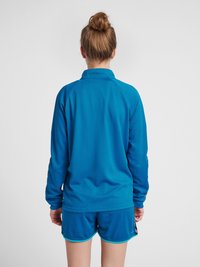 Blauwe sportoutfit met een langgeschouderd shirt met een textuurpatroon en shorts met contrasterende afwerking. Achteraanzicht toont de ontspannen pasvorm en de mouwen.