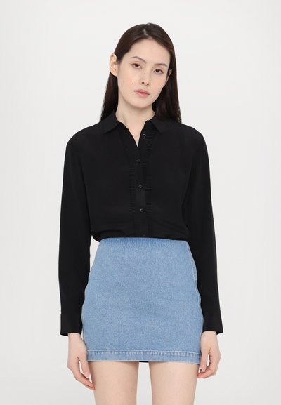 Black long-sleeve blouse with button closure and ruffled detail, paired with a light blue denim mini skirt. Smooth fabric and fitted design.