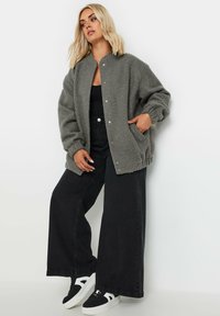 Överdimensionerad grå fleecejacka med tryckknappar, ribbade ärmslut och framfickor, matchad med högmidjade svarta jeans och svarta sneakers.