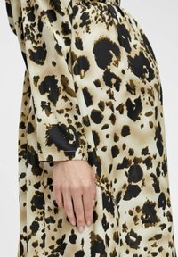Satiini mekko, jossa on abstrakti eläinkuoski beige, musta ja ruskea väri, pitkät hihat ja rento mitoitus, korostaen pehmeää rakennetta.