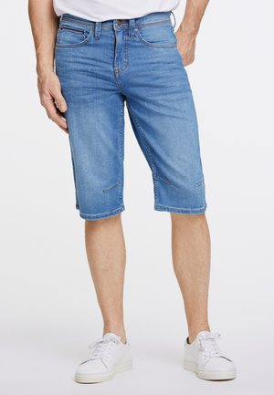Pantalones cortos cargo de mezclilla en azul claro con corte recto, dobladillo a la altura de la rodilla, bolsillos frontales y sutiles detalles de costura. Combinados con zapatillas blancas.
