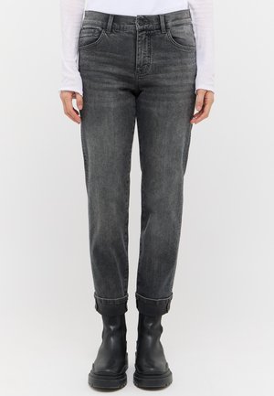 Person wearing rolled-up dark gray jeans, black chunky boots, and a white long-sleeve top, standing against a plain background.