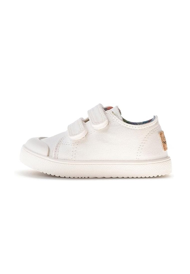 Zapatilla de lona blanca de corte bajo con dos correas de velcro, suela de goma texturizada y punta redondeada sobre un fondo blanco.