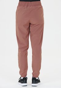 Leichte, rosa Nylon-Hosen mit einem elastischen Bund und schmal zulaufenden Beinen, ausgestattet mit Knöchelbündchen, kombiniert mit schwarzen Turnschuhen.