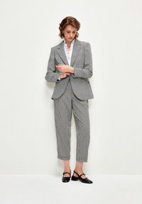 Harmaa ruutulevybleiseri, joka on yhdistetty matching lyhyisiin housuihin, joissa on teksturoitu pinta. Kera valkoisen röyhelöblousin ja mustien kenkien.