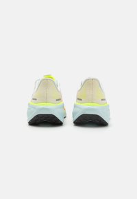 Zapatos de running con parte superior de malla en blanco y acentos en amarillo neón, suelas acolchadas con una entresuela de color turquesa y suelas exteriores de goma negra.