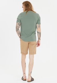 Vihreä lyhythihainen t-paita, joka on yhdistetty khaki-shortsien kanssa, joissa on käärityt hihat. Rento jalkine täydentää asun.