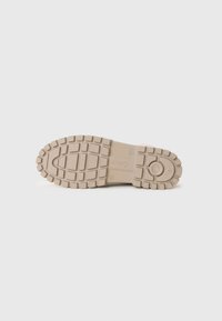 Suela de zapato de goma de color beige claro con un patrón texturizado y profundas ranuras para tracción. Incluye un detalle de logo circular en el centro.
