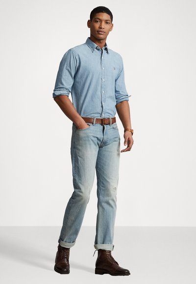 Light blue denim shirt with button-down collar, paired with distressed light blue jeans and brown leather lace-up boots. Brown belt accentuates waist.