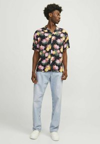 Camisa de manga corta negra con flores en tonos rosa y amarillo; combinada con jeans de mezclilla azul claro y zapatillas blancas. Estilo casual, corte holgado.