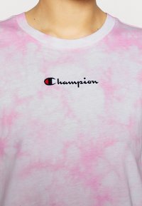 Różowa koszulka bawełniana tie-dye z haftowanym logo "Champion" w kolorze czarnym, okrągłym kołnierzykiem i miękką fakturą.