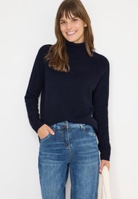 Pull à col roulé bleu marine avec des détails côtelés sur les épaules, assorti à un jean en denim bleu clair, avec une texture légère partout.
