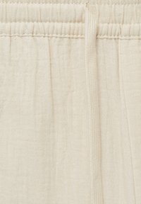 Tissu couleur crème avec une texture froissée, comprenant une taille élastique et un cordon de serrage pour un ajustement. Design minimaliste.