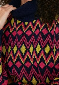 Sweter dziany z golfem i geometrycznym wzorem w kolorach różowym, żółtym i granatowym, wykonany z teksturowanej tkaniny o luźnym kroju.