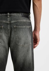 Ciemnoszare dżinsy z denimu z efektem sprania, wyposażone w standardowe tylne kieszenie oraz czarną skórzaną naszywkę z logo na pasku od spodni.