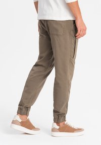 Khaki joggingsbroek met elastische boorden, zijzak en een soepele katoenen mix. Gepaard met bruin en witte lage sneakers.
