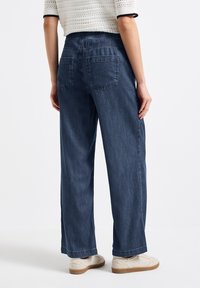 Ciemnoniebieskie dżinsy typu wide-leg z elastycznym paskiem w talii, z dwiema tylnymi kieszeniami i miękką teksturą denimu.