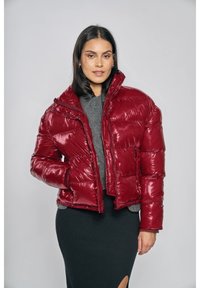 Röd pufferjacka med glansig yta, kort design, hög krage och dragkedja. Kombinerad med en mörk, figursydd kjol och en grå topp.