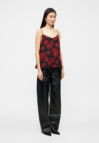 Μαύρο αμάνικο τοπ με κόκκινο τύπωμα τριαντάφυλλου, συνδυασμένο με ψηλόμεσα, λαμπερά μαύρα παντελόνια από πατινέ δέρμα. Απλός σχεδιασμός, ίσια εφαρμογή.
