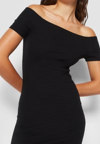 Czarna sukienka bez ramiączek z krótkimi rękawami, prążkowana tekstura, dopasowany krój i gładki materiał podkreślający smukłą sylwetkę.