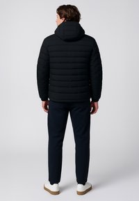 Giacca a vento nera con motivo a righe orizzontali, cappuccio e maniche lunghe. Indossata con pantaloni blu navy e sneakers bianche.