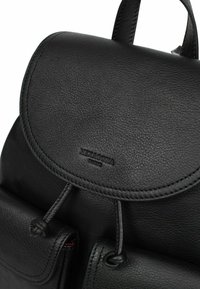 Zaino in pelle nera con patta arrotondata, finitura texturizzata, chiusura a coulisse e tasca anteriore con un branding discreto.