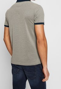 Koszulka polo w jasnoszarym kolorze z granatowym kołnierzykiem i akcentami na rękawach, wykonana z teksturowanej tkaniny i w dopasowanym kroju. Widok z tyłu.