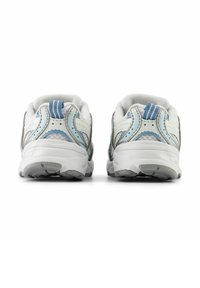 Scarpe da ginnastica bianche e azzurro chiaro viste da dietro, con suole grigie aderenti e linguette, su sfondo bianco.