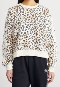 Leopardmönstrad sweatshirt med elastiska manchetter och nederkant, beige och svarta färger, har vita adidas-ränder på ärmarna.
