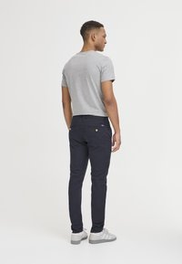 Siva pamučna majica, uske tamnoplave hlače, tenisice s sivim i bijelim detaljima. Ima stražnje džepove s detaljem gumba.