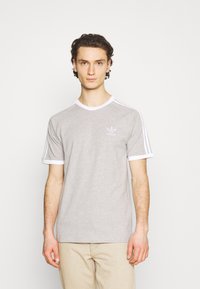 Pilkas medvilnės marškinėliai su apvaliu kaklu, baltais akcentais ant rankovių ir apykaklės, bei maža balta Adidas logotipas ant krūtinės.