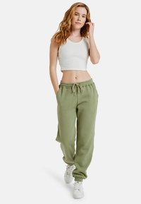 Olijfgroene sweatpants met elastische tailleband en trekkoord, gecombineerd met een witte geribde crop top en witte sneakers. Comfortabele pasvorm.