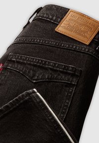 Zwarte denim jeans met een leren patch en meerdere zakken. Heeft een contrasterende witte steekdetail langs de zoom.