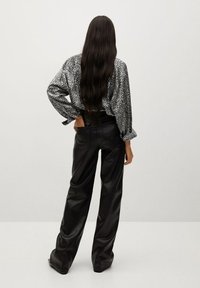 Chemise à motifs noir et blanc à manches longues, associée à un pantalon en cuir noir taille haute, vue de dos.