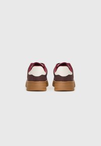 Brown and burgundy sneakers with white accents, textured rubber soles, and padded collars, featuring a low-profile design.