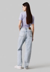 Camiseta corta de color púrpura claro y jeans de tiro alto azul claro con una etiqueta de cuero beige, combinados con zapatillas blancas, mostrando un atuendo casual.