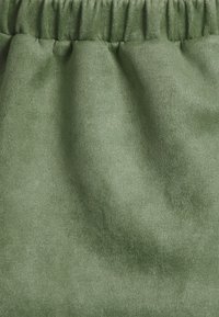 Tecido verde e suave com uma textura lisa, apresentando um design franzido na parte superior. Brilho sutil e cor consistente em toda a superfície.