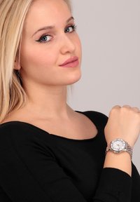 Orologio da polso argento con quadrante bianco, cinturino in metallo e caratteristiche cronografiche, indossato sul polso di un modello con una maglietta nera.