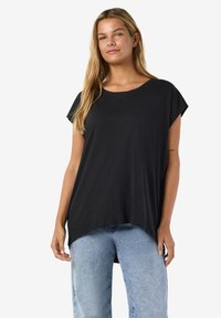 Tricou negru cu mâneci scurte, cu decolteu rotund și croială lejeră. Țesătura pare ușoară și ușor texturată. Purtat împreună cu blugi bleu deschis.