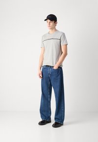 Gray cotton t-shirt with black text, paired with loose blue denim jeans and black shoes. Model wears a black cap. Simple design.