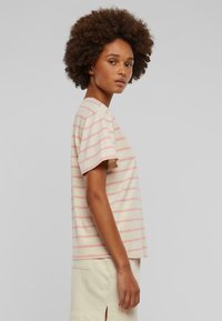T-shirt w paski w kremowym kolorze z różowymi poziomymi paskami, krótki rękaw, luźny krój, okrągły dekolt, wykonany z miękkiego materiału o gładkiej teksturze.
