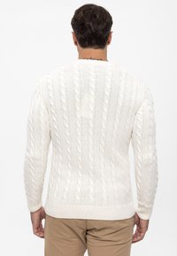 Jersey blanco de punto con trenzas que presenta un dobladillo y puños acanalados, con un patrón texturizado. La vista posterior muestra un diseño sólido y sin costuras.